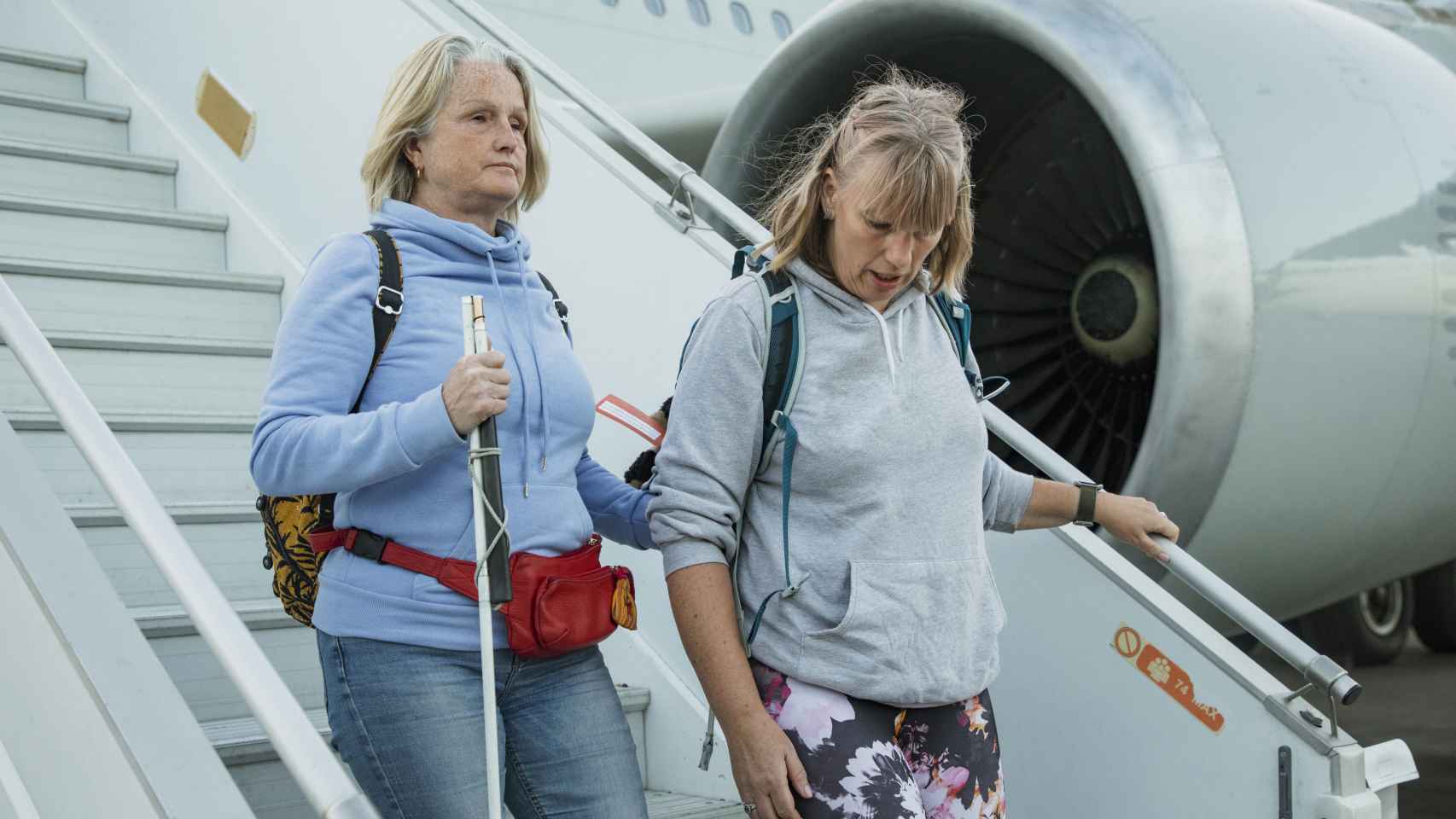 Dos mujeres, una de ellas invidente, bajan por las escalerillas de un avión