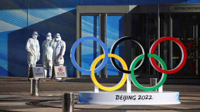 Tres sanitarios con traje EPI en pie observan los anillos olímpicos en Pekín, China.
