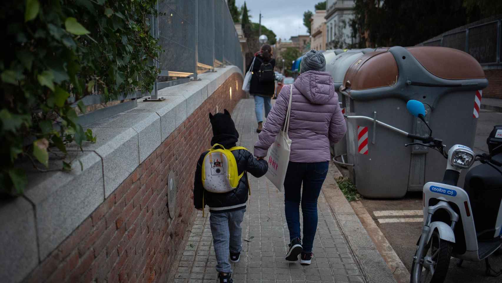 Una mujer lleva de la mano a un niño a su primer día de clase presencial tras la Navidad.