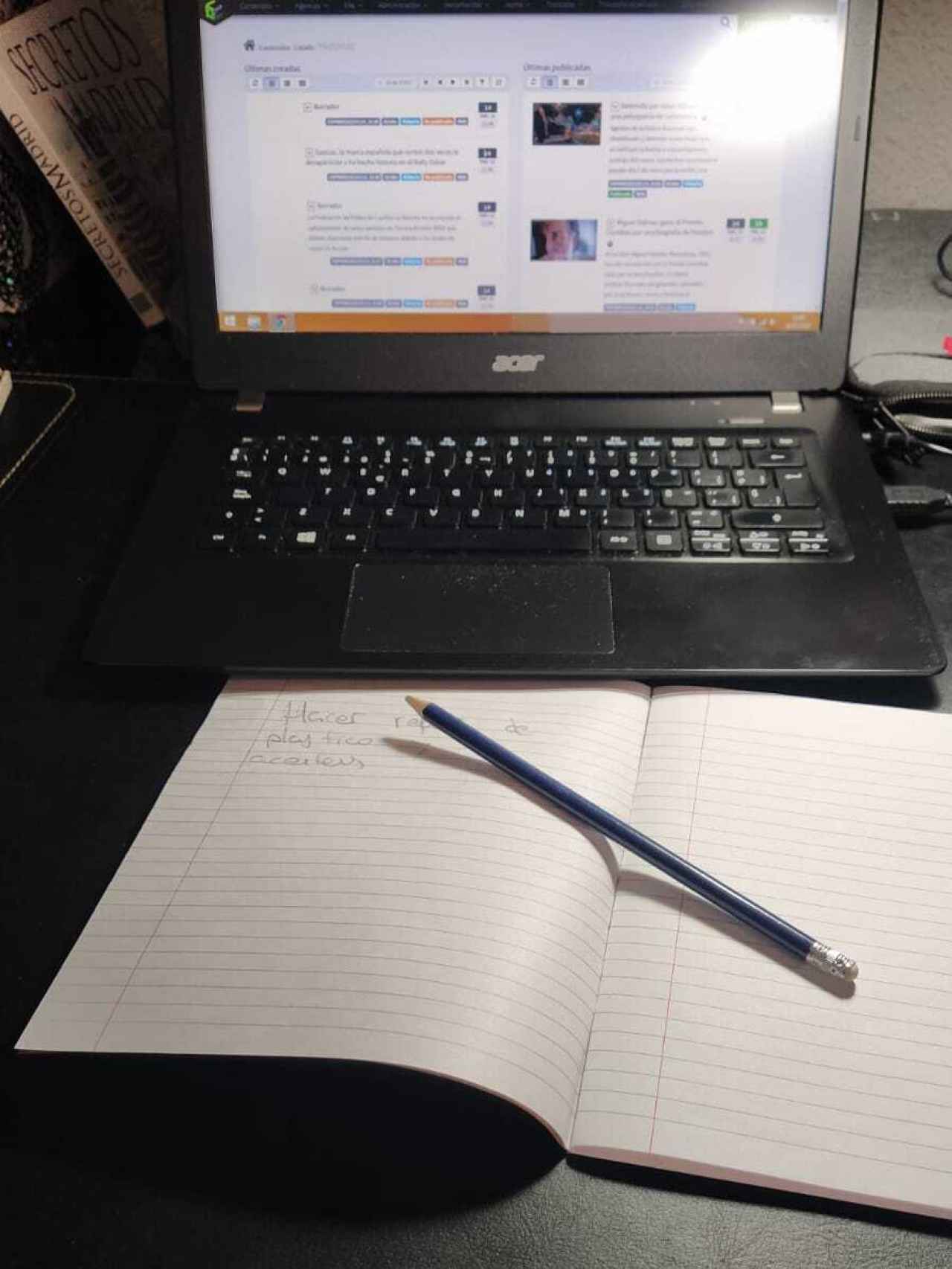 La libreta de papel y cartón y el lápiz empleados para apuntar. De fondo, el ordenador.
