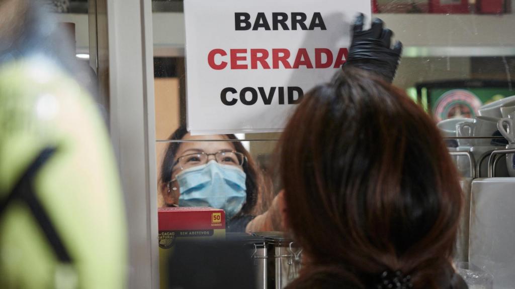 Un camarera coloca un cartel de barra cerrada por Covid