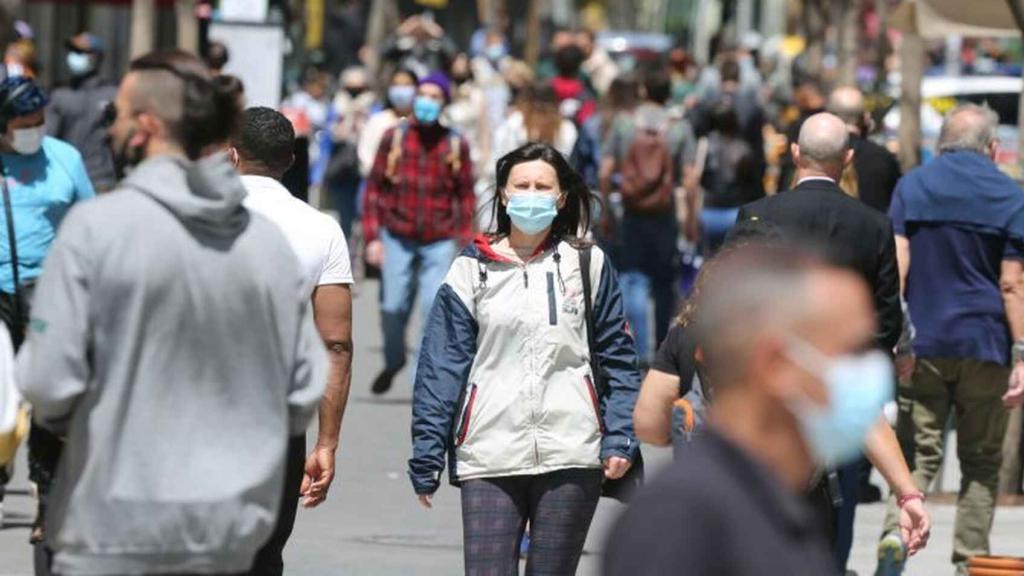 Una mujer camina por la calle con la mascarilla puesta.