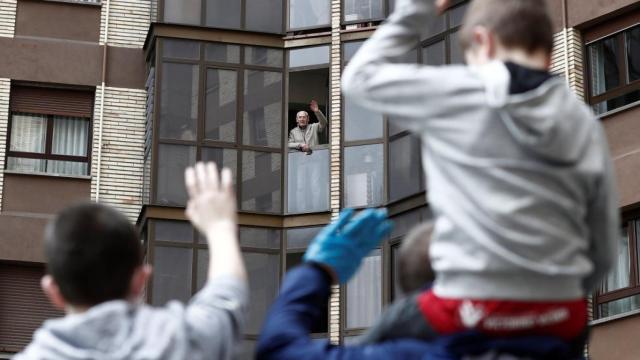 Dos niños saludan desde la calle a su abuelo, en imagen de archivo.