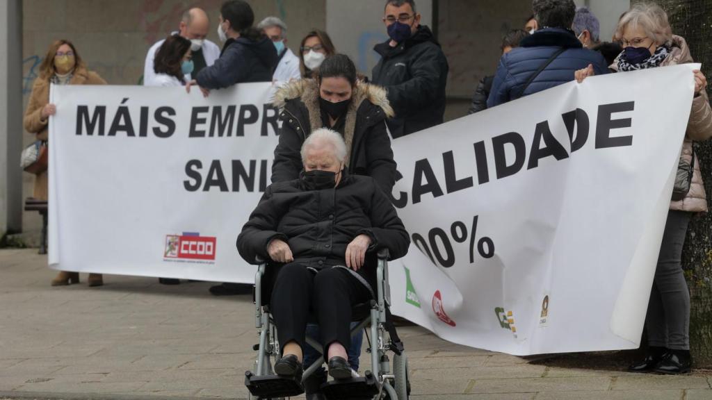 Una mujer en silla de ruedas pasa por delante de varios sanitarios que protestan, con una pancarta que reza ‘Más empleo y de más calidad. Sanidad Pública 100%’.