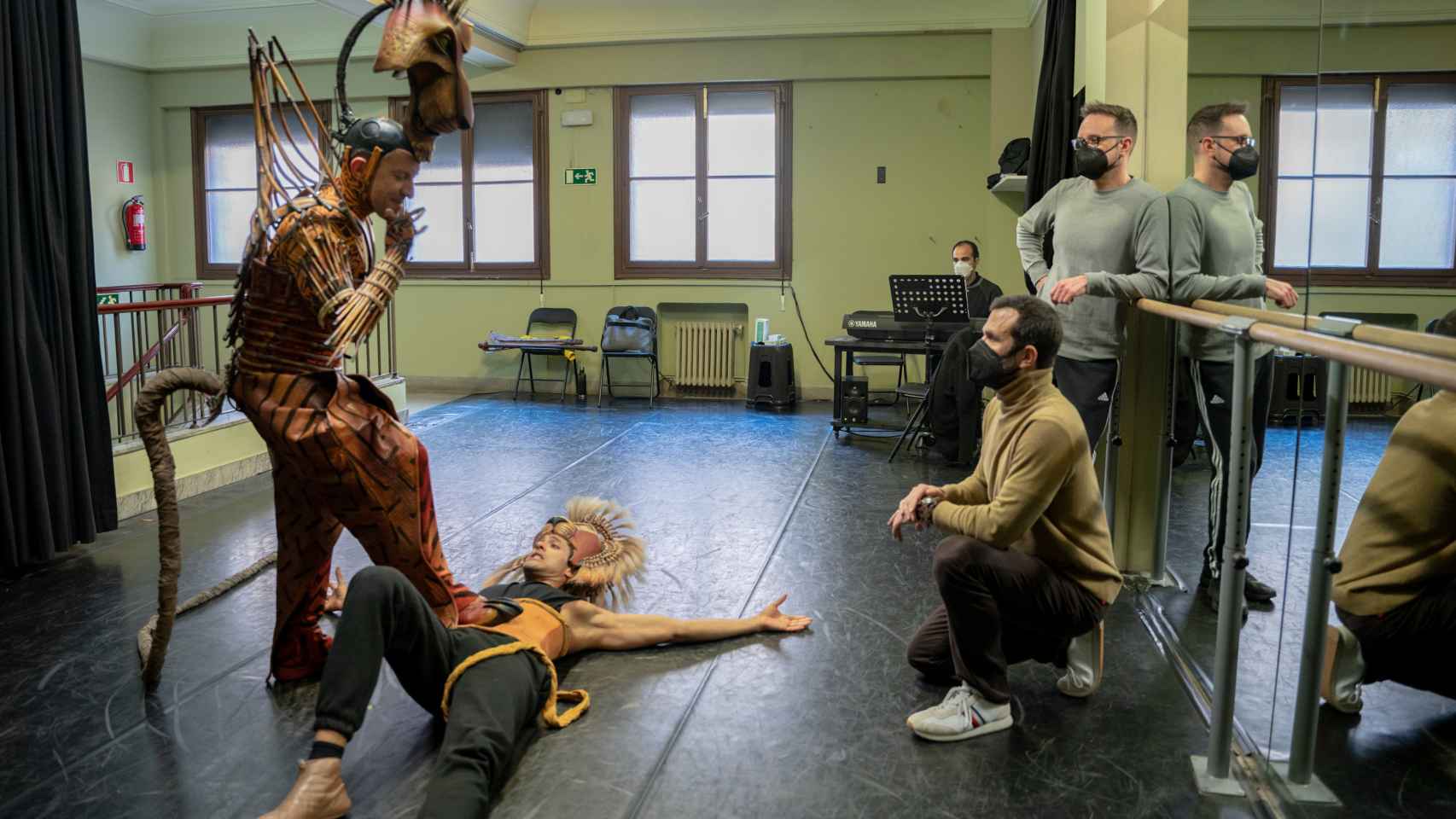 Zenón Recalde, agachado, observa y dirige el ensayo de los actores de Scar y Simba.