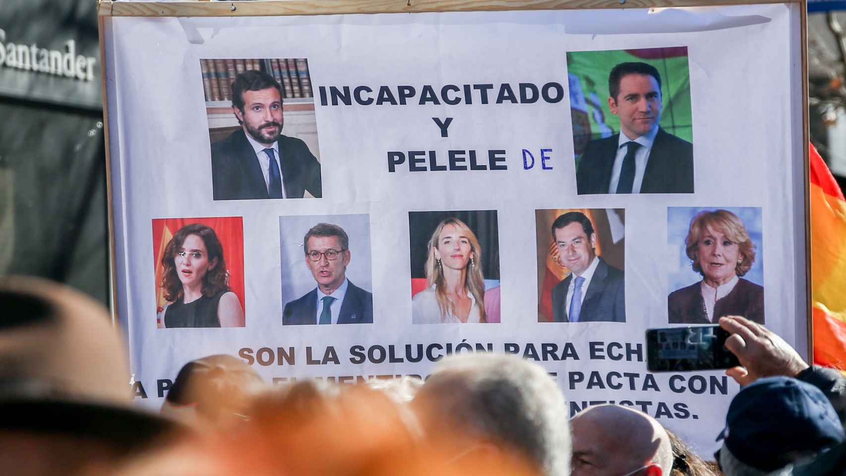 Varios manifestantes sostienen una pancarta con imágenes de miembros del PP en la concentración de apoyo a Díaz Ayuso celebrada este domingo en Génova 13.