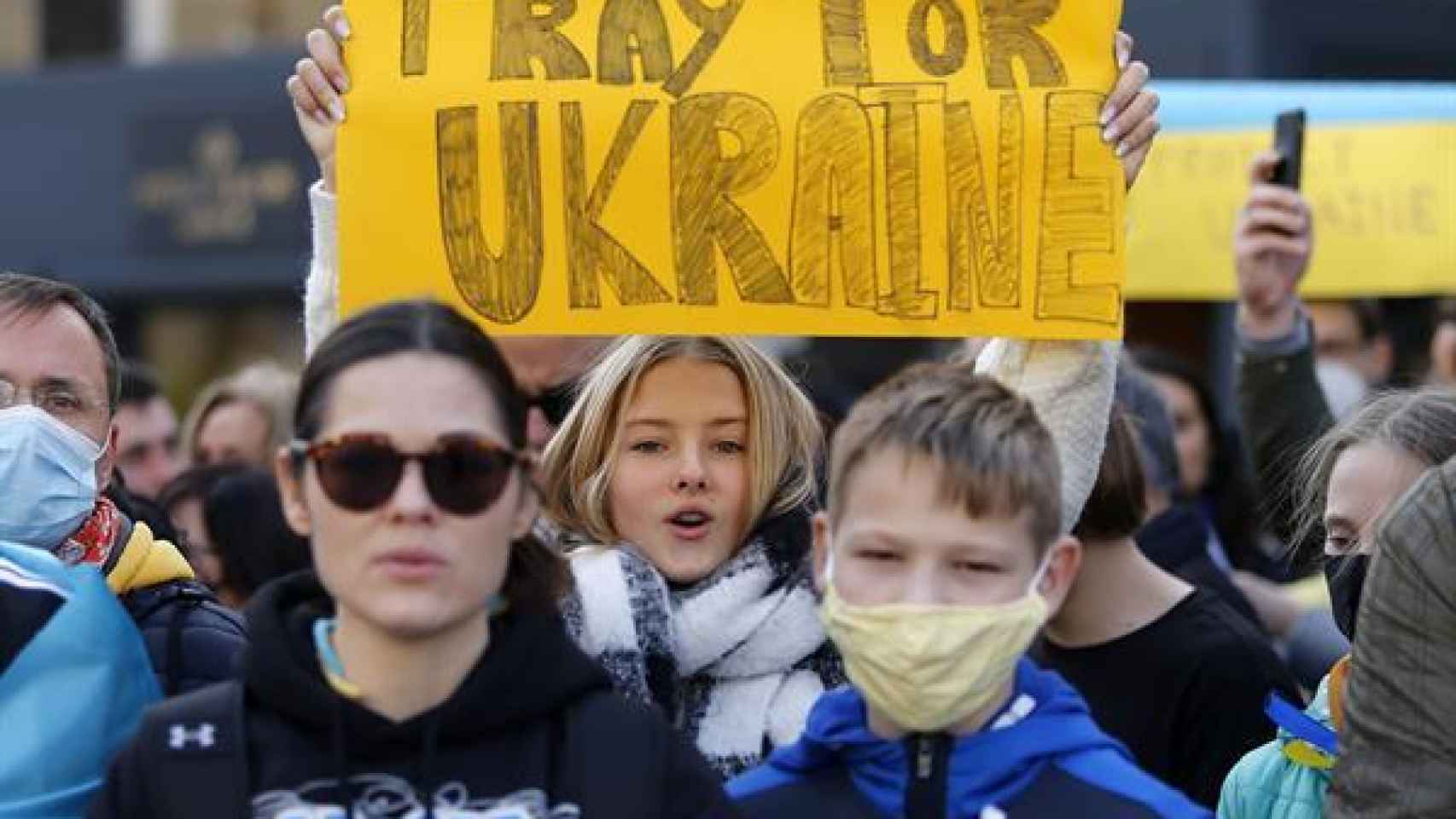 Entre los numerosos manifestantes, una chica porta un cartel que dice en inglés 'Rezad por Ucrania.