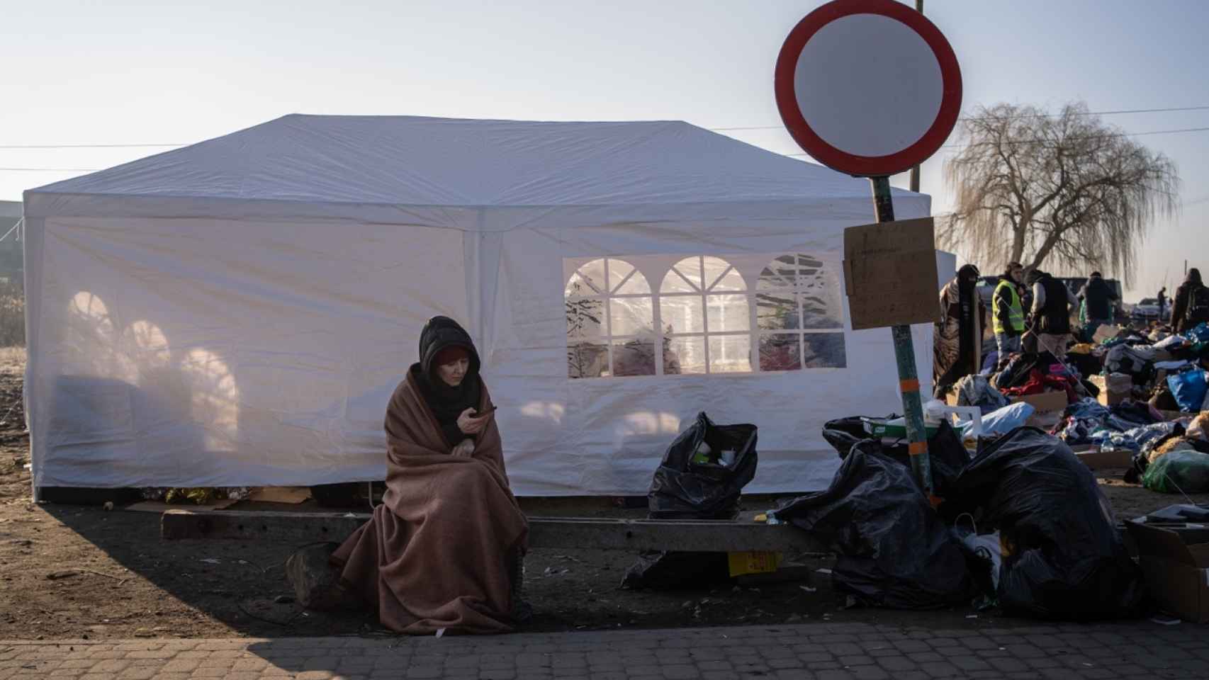 Cubierta por una manta por las bajas temperaturas, una mujer avisa a sus familiares que ha logrado llegar a Polonia.