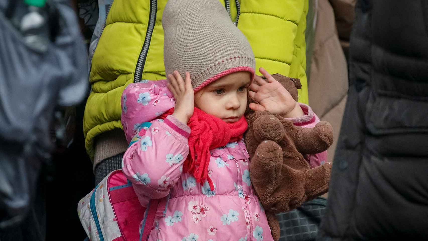 Una niña se tapa los oídos por las alarmas antiaéreas mientras espera para embarcar en un tren que la saque de Kiev.