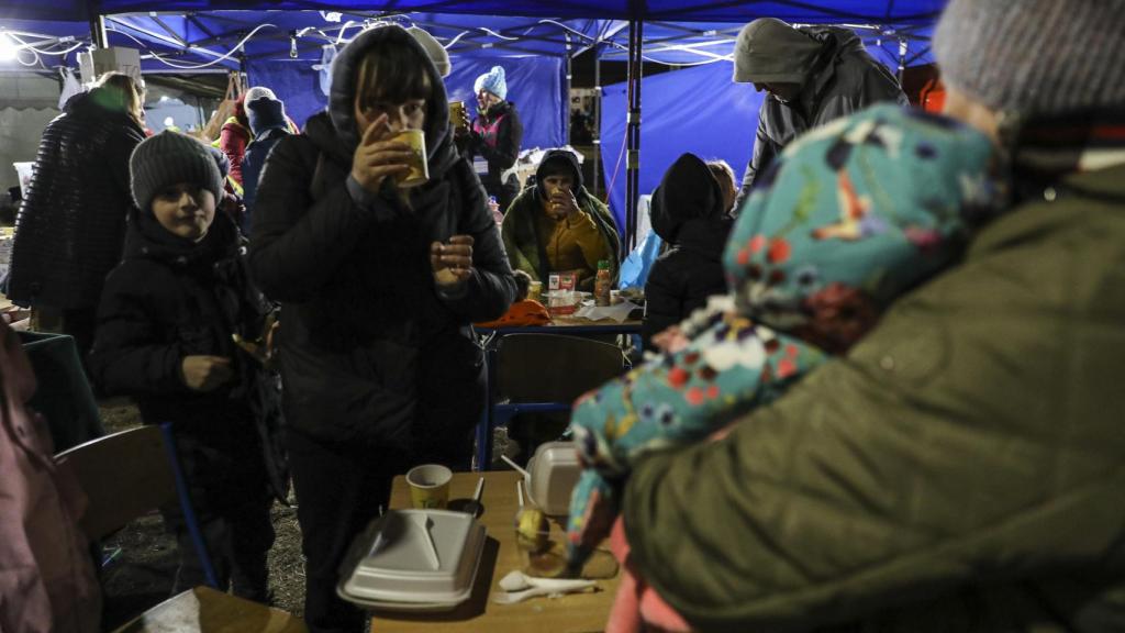 Refugiados comen y esperan el transporte fuera del centro de refugiados habilitado en Przemysl, Polonia.