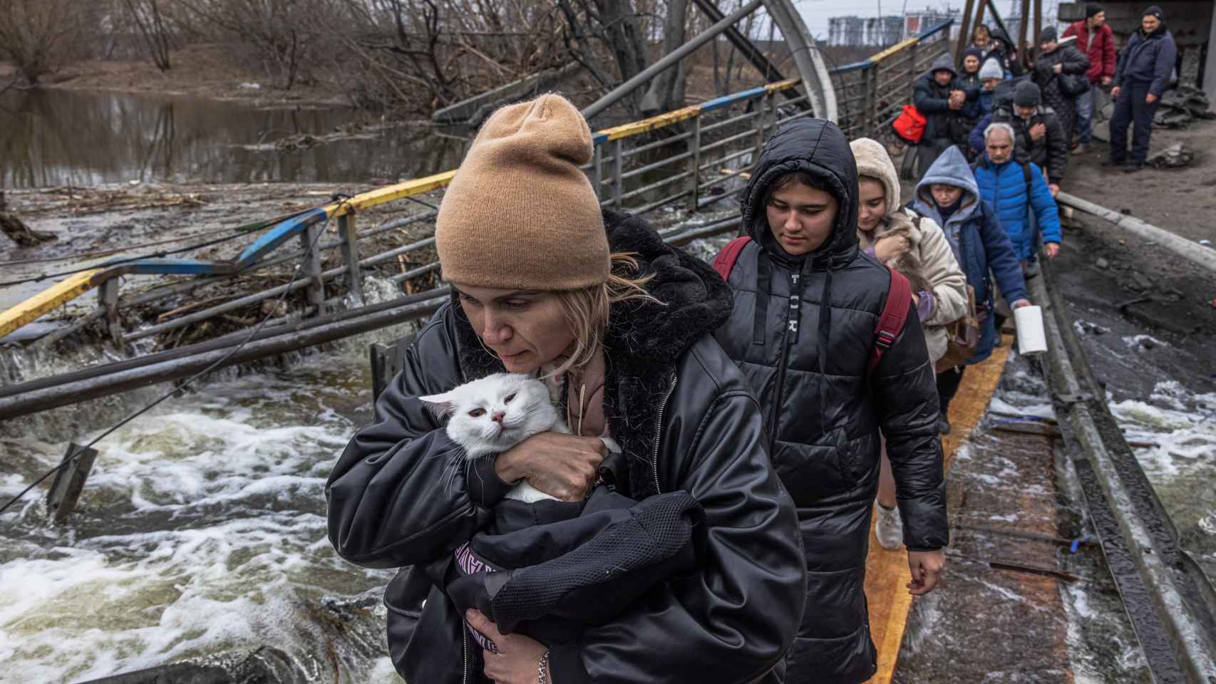 Una mujer con su gato cruza un puente destruido mientras los residentes huyen desde el frente de la ciudad de Irpín, en Kiev, este lunes