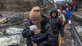 Una mujer con su gato cruza un puente destruido mientras los residentes huyen desde el frente de la ciudad de Irpín, en Kiev, este lunes