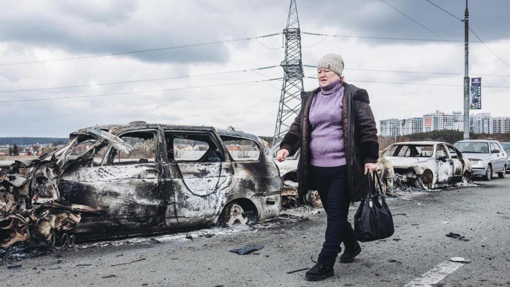 Una mujer camina delante de unos coches quemados en un puente de Irpin (Ucrania).