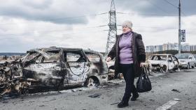 Una mujer camina delante de unos coches quemados en un puente de Irpin (Ucrania).