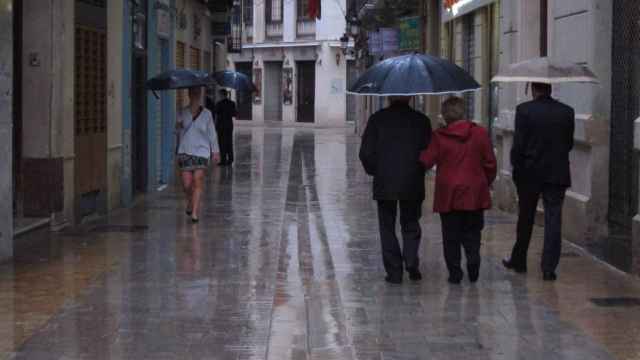 Varias personas caminan por una calle de Málaga mientras llueve.
