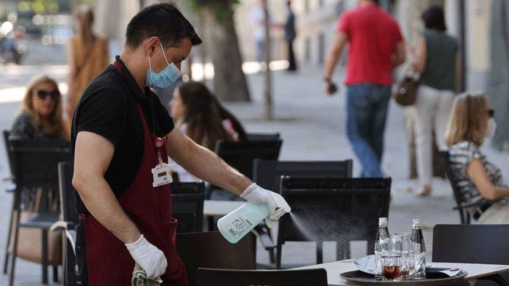 Un camarero desinfecta una mesa en la terraza de una cafetería