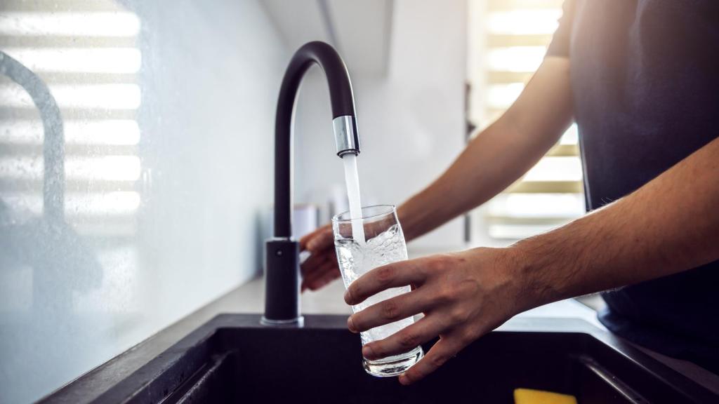 Un hombre bebe un vaso de agua del grifo.