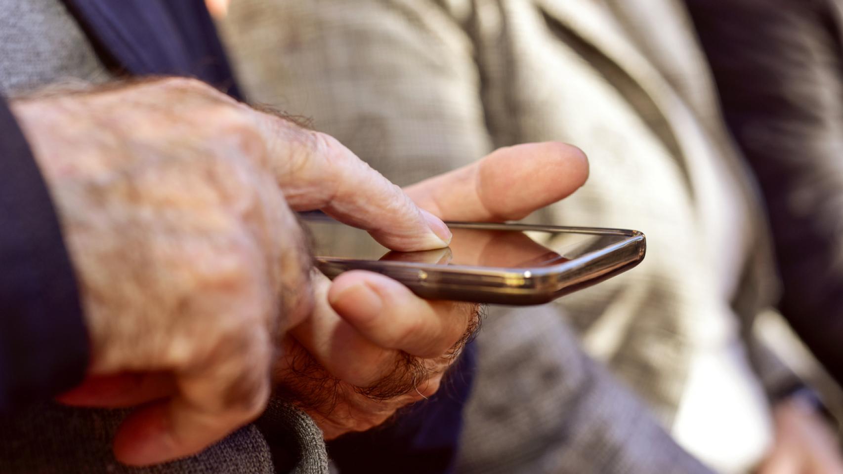 Un anciano pulsa la pantalla de un teléfono móvil con su dedo
