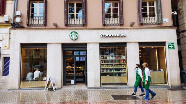 Imagen de dos empleadas del nuevo Starbucks de la Plaza de la Constitución, en Málaga, pasando junto al establecimiento.