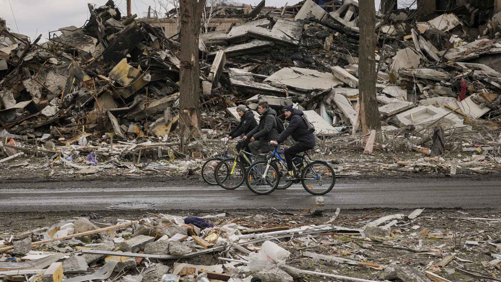 Tres civiles ucranianos pasean en bicicleta entre los escombros.