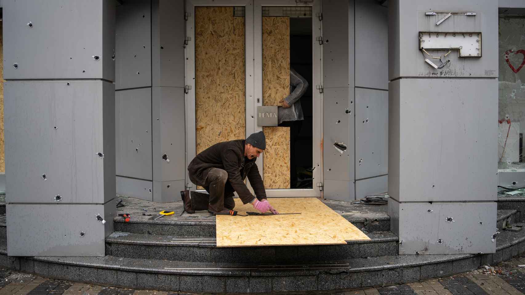 Vladimir mide y recorta la madera para proteger su tienda de ropa. El ataque de hoy ha roto sus cristales y dañado la fachada.