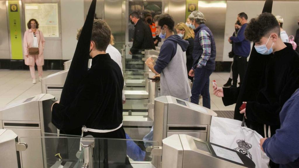 Dos jóvenes nazarenos pasan por el acceso de una de las estaciones del Metro de Málaga.