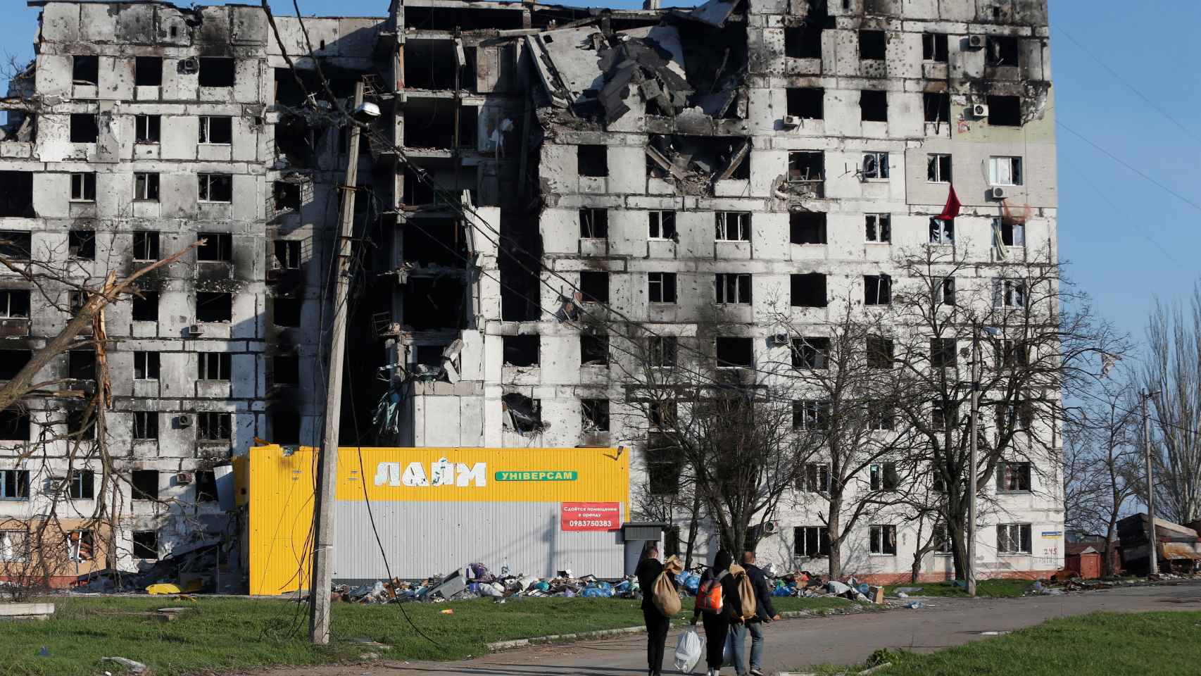 Residentes caminan delante de un edificio destruido en Mariúpol.
