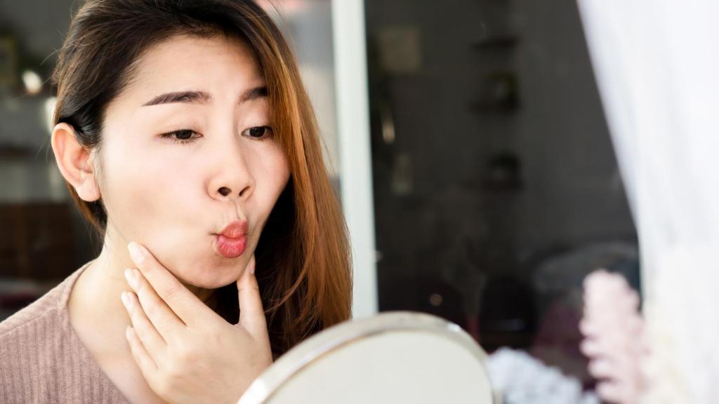 Una mujer practica ejercicios faciales frente al espejo.