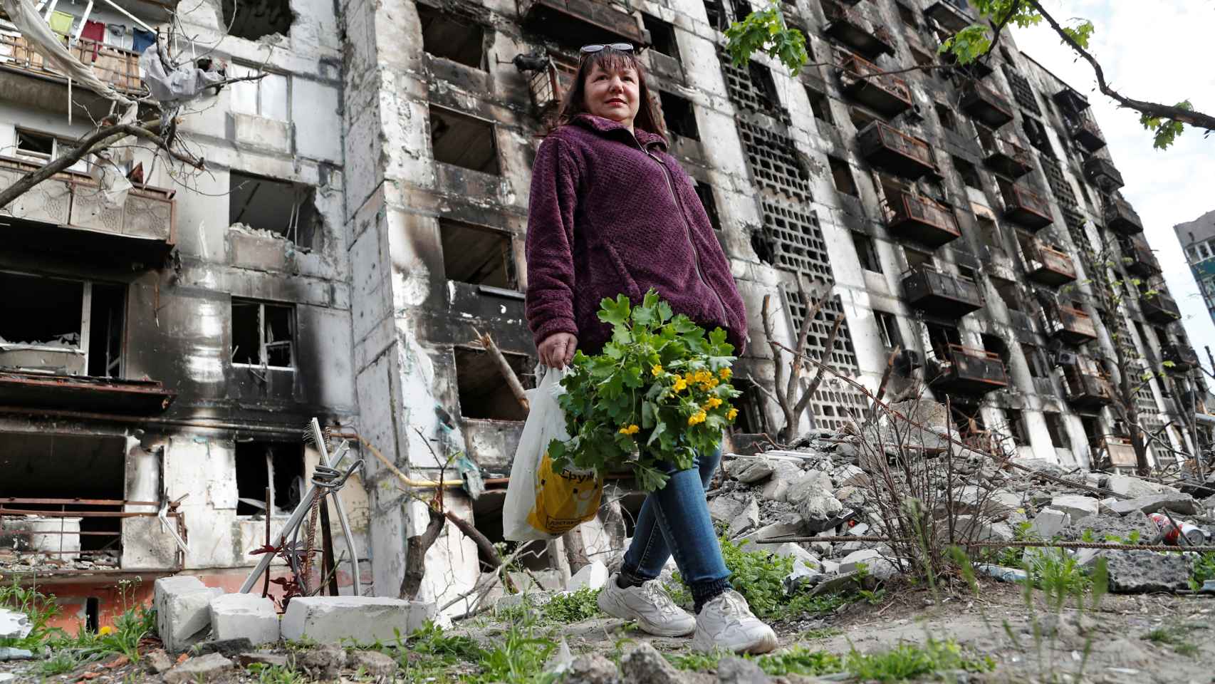 Una mujer con un ramo de flores delante de un edificio destruido en Mariúpol.