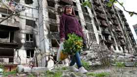 Una mujer con un ramo de flores delante de un edificio destruido en Mariúpol.