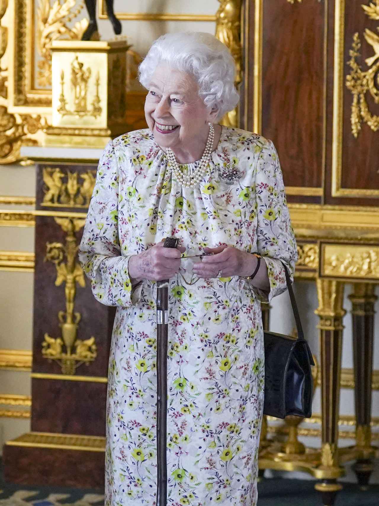 La reina Isabel II apoyada en un bastón.