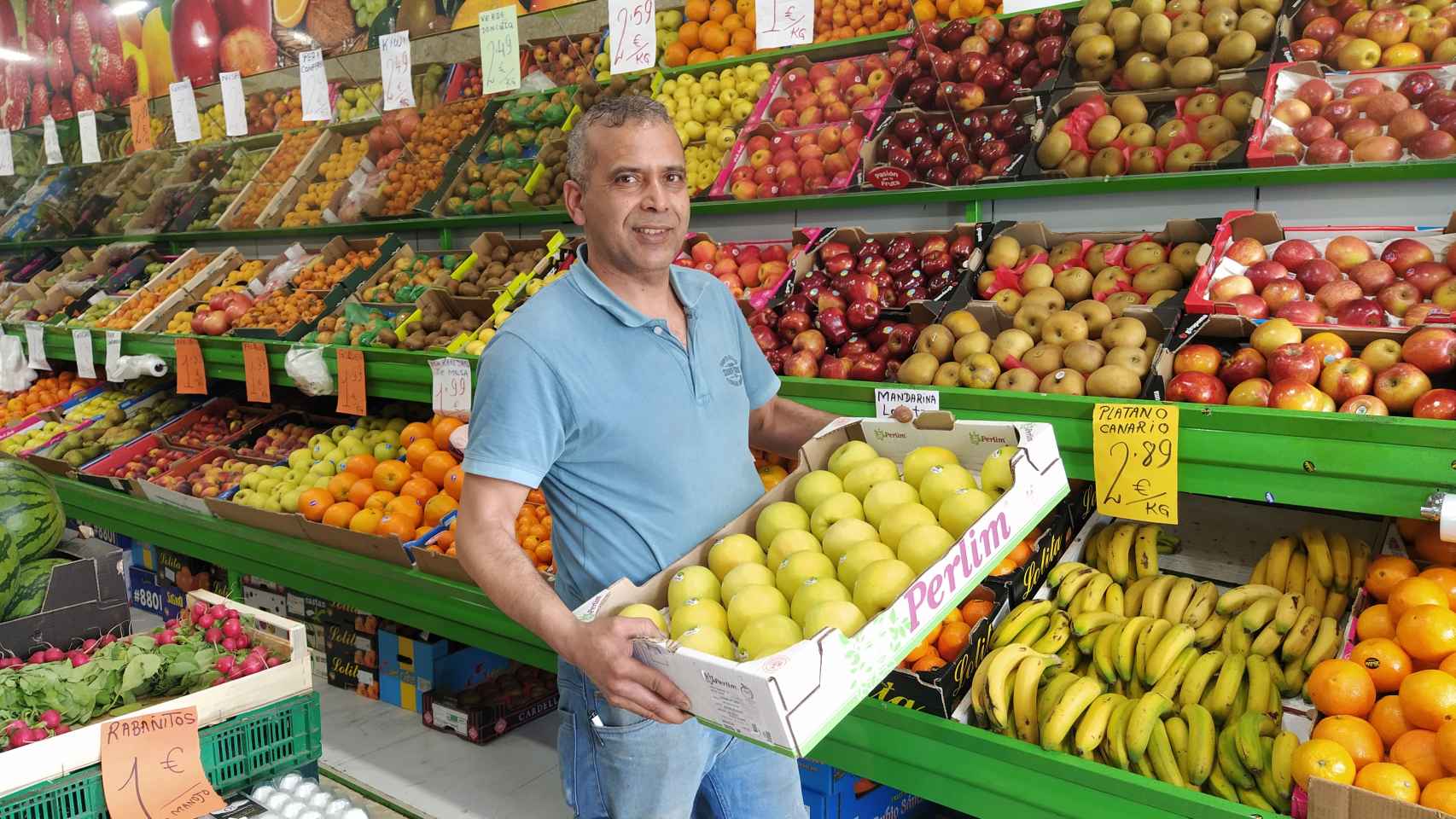 Amal, un frutero marroquí, sostiene una caja de manzanas en su frutería de barrio.