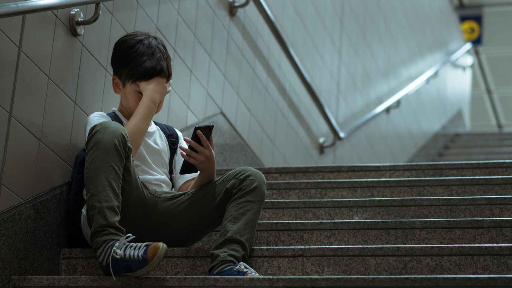 Un niño sentado en unas escaleras y conectado a las redes sociales. Imagen de archivo.