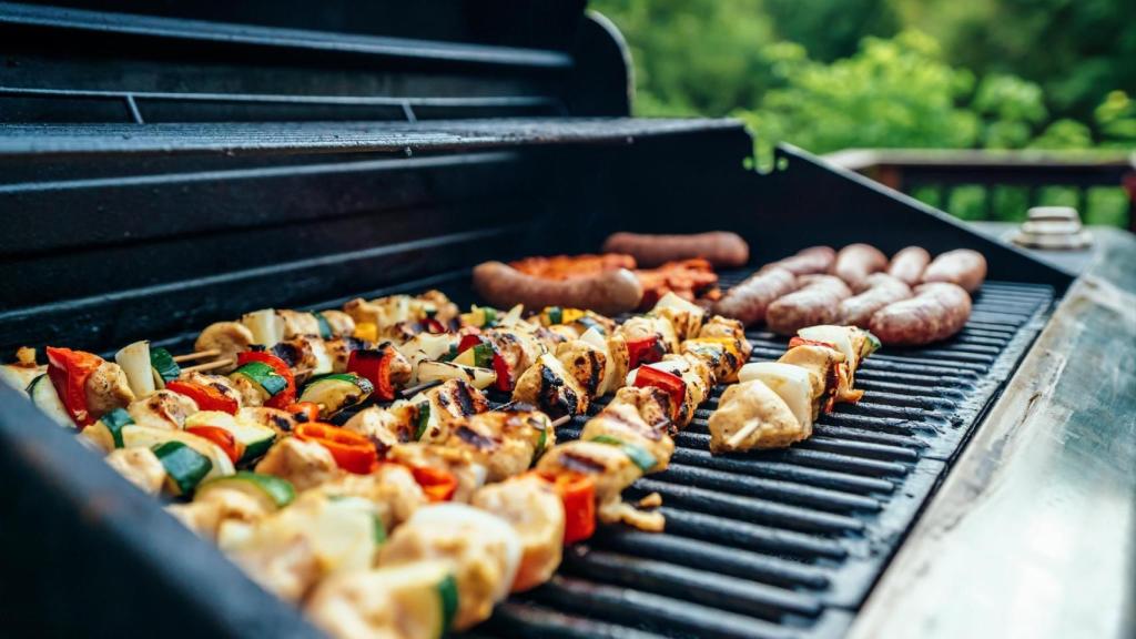 Un hombre cocina unas hamburguesas en la barbacoa.