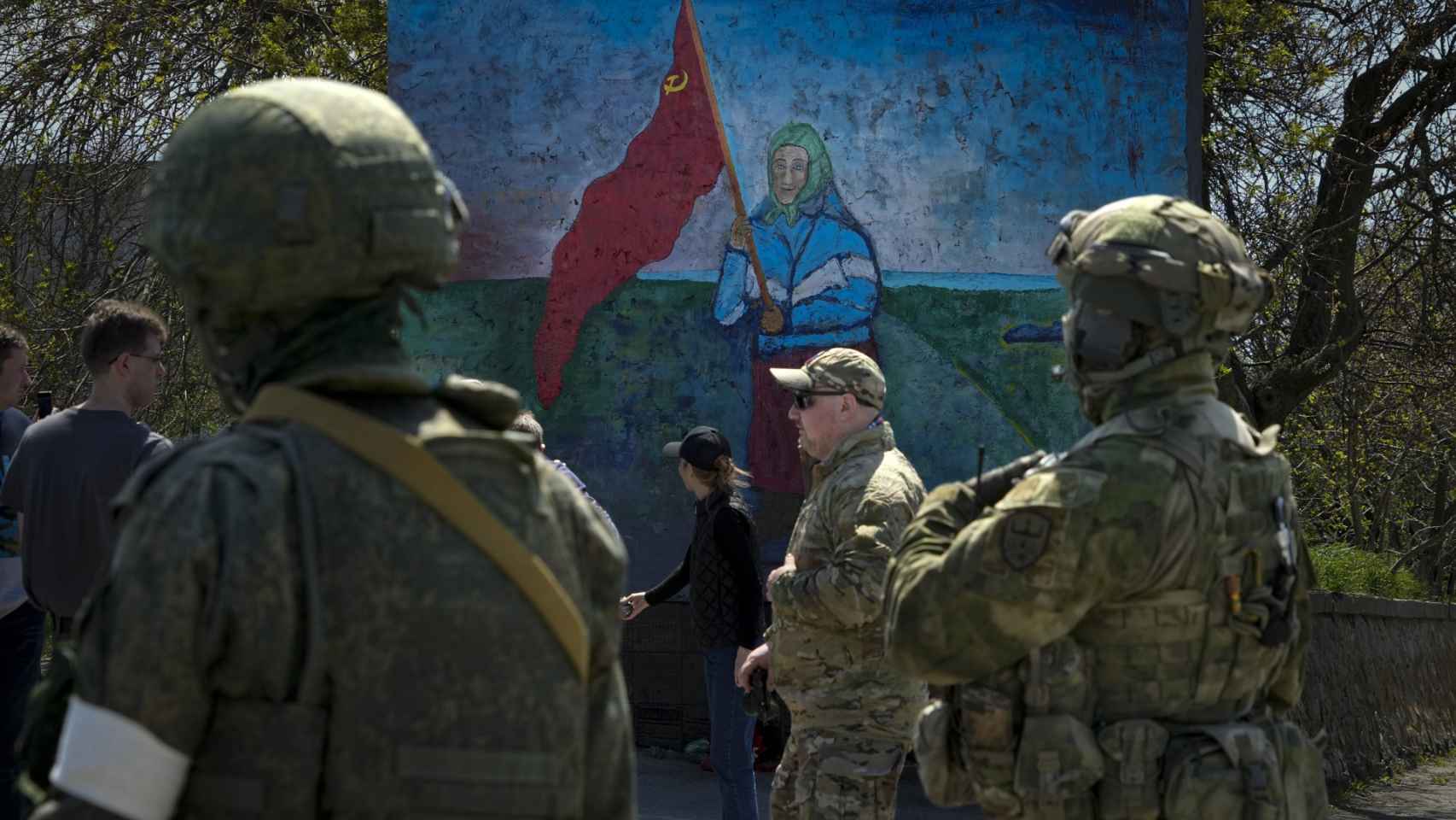 Soldados rusos se paran cerca de una pintura de una mujer ucraniana que sostiene una bandera roja de la era soviética en territorio bajo el gobierno de la República Popular de Donetsk.