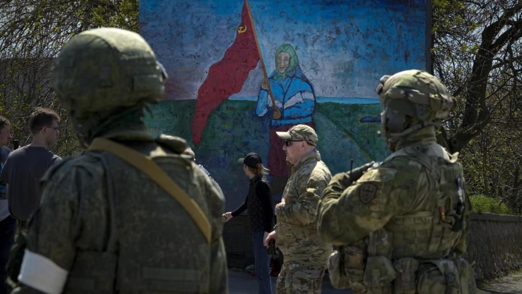 Soldados rusos se paran cerca de una pintura de una mujer ucraniana que sostiene una bandera roja de la era soviética en territorio bajo el gobierno de la República Popular de Donetsk.
