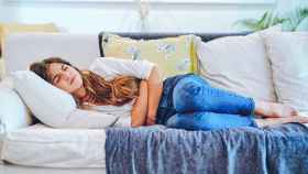 Una mujer joven acostada en un sofá sufre fuertes dolores menstruales.