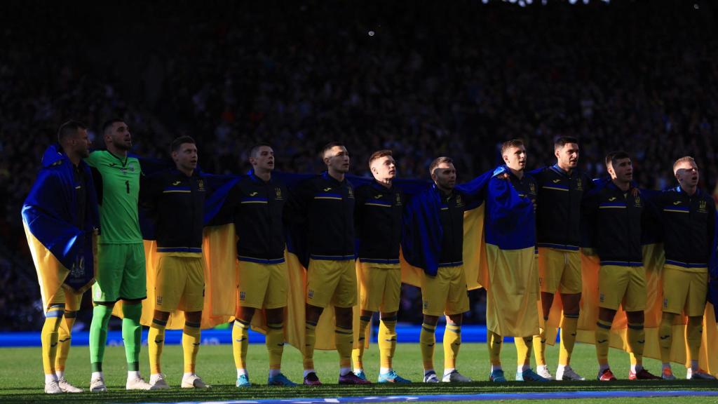 Los jugadores de la selección de Ucrania, escuchando el himno con su bandera sobre los hombros