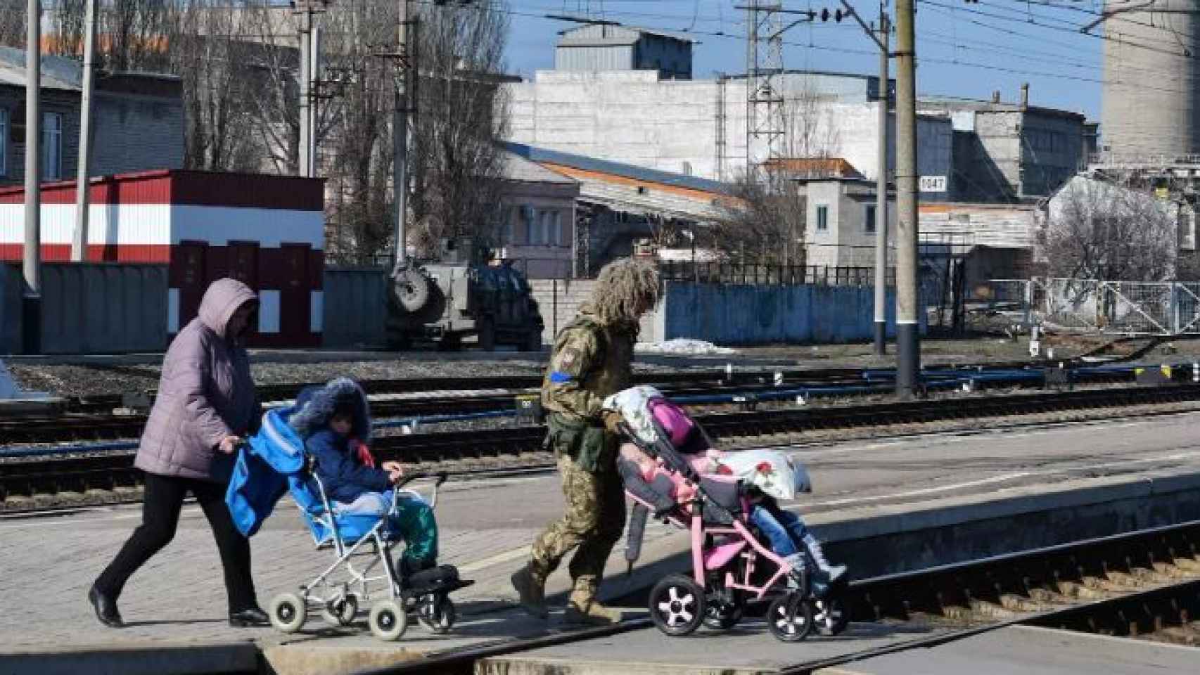 Una mujer y un militar son vistos ayudando a varios niños a subirse a un tren.