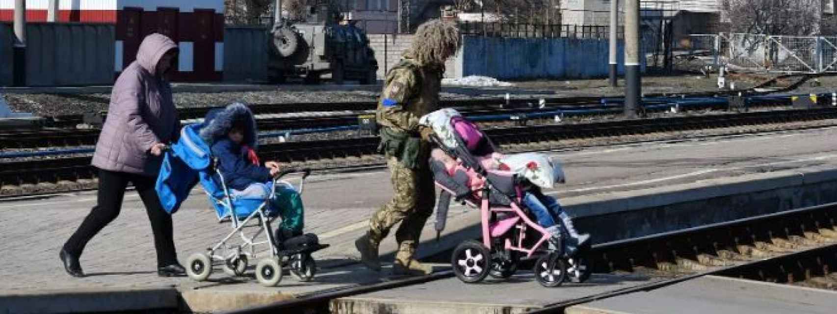 Una mujer y un militar son vistos ayudando a varios niños a subirse a un tren.
