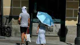 Personas se cubren del sol con gorra y sombrilla.