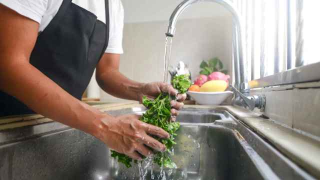 Una persona lava una verdura bajo el grifo de la cocina.