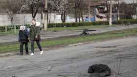 Natasha Grebenkina y su hijo pasan junto a cuerpos de civiles cerca de una parte destruida en Mariúpol.