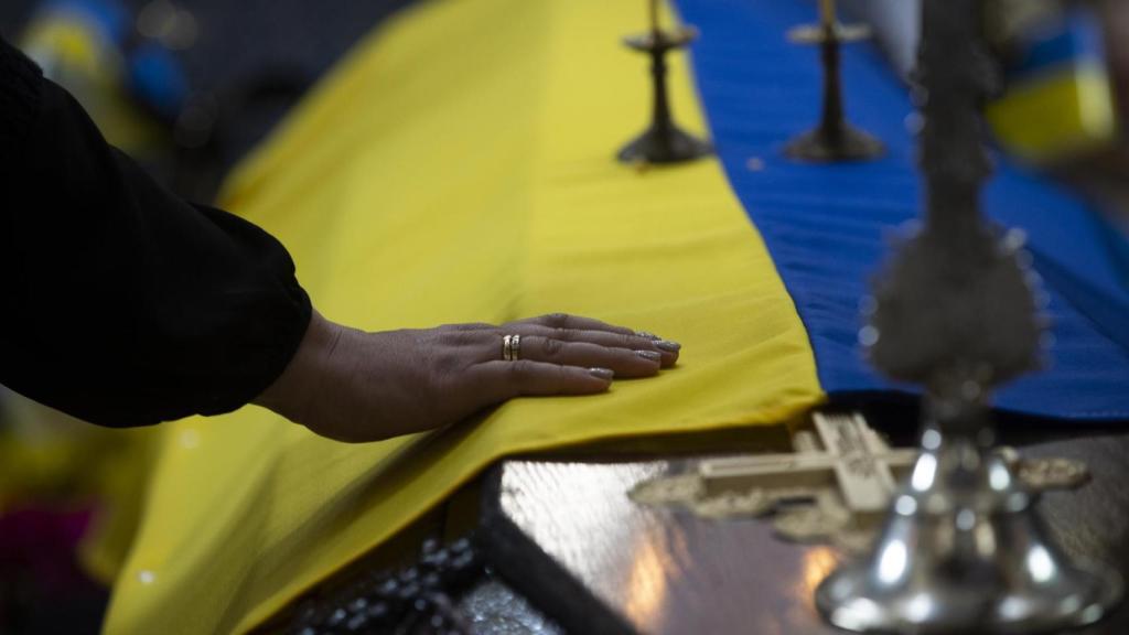 Una persona toca la bandera ucraniana sobre el féretro de un soldado ucraniano.