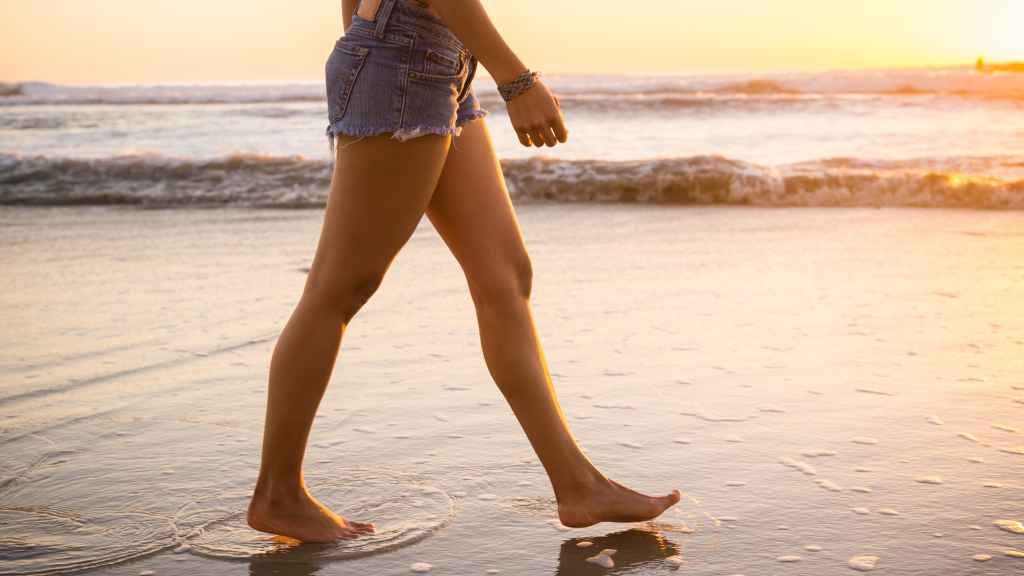 Las piernas de una mujer caminando por la playa.