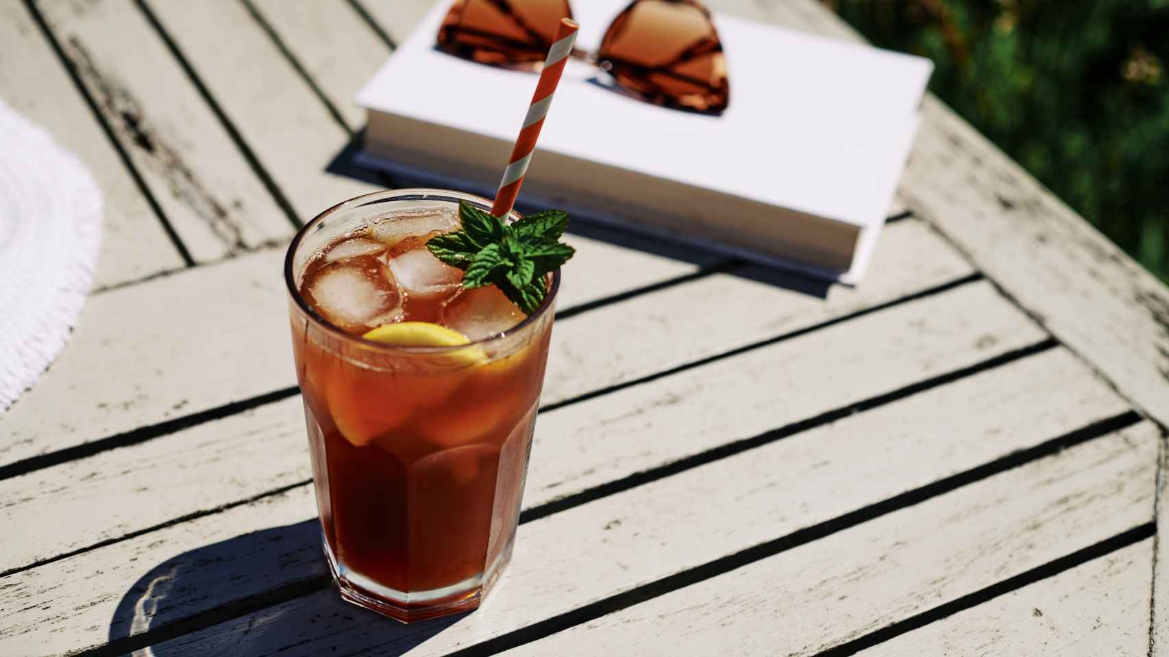 Un té helado sobre una mesa junto a unas gafas de sol y un libro.
