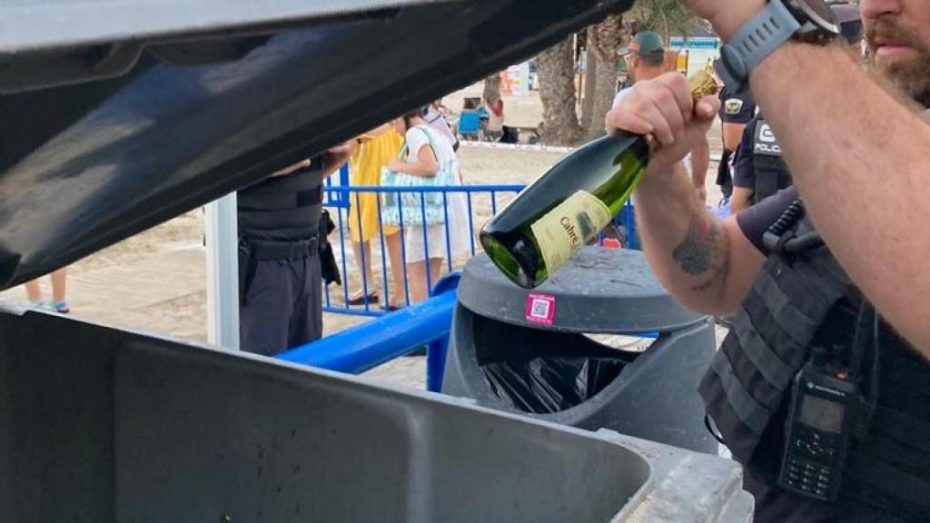 Un agente deposita en un contenedor una botella de alcohol requisada.