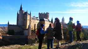 Imagen de unos viandantes en Segovia con el Alcázar al fondo