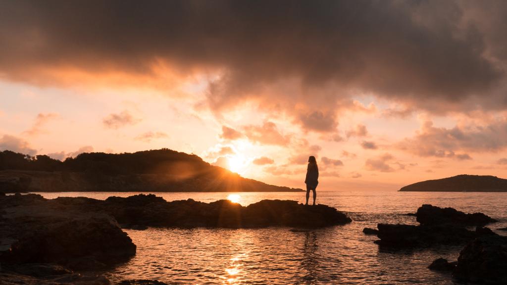 Una mujer ve la puesta de sol en Es Vedrá, Ibiza.