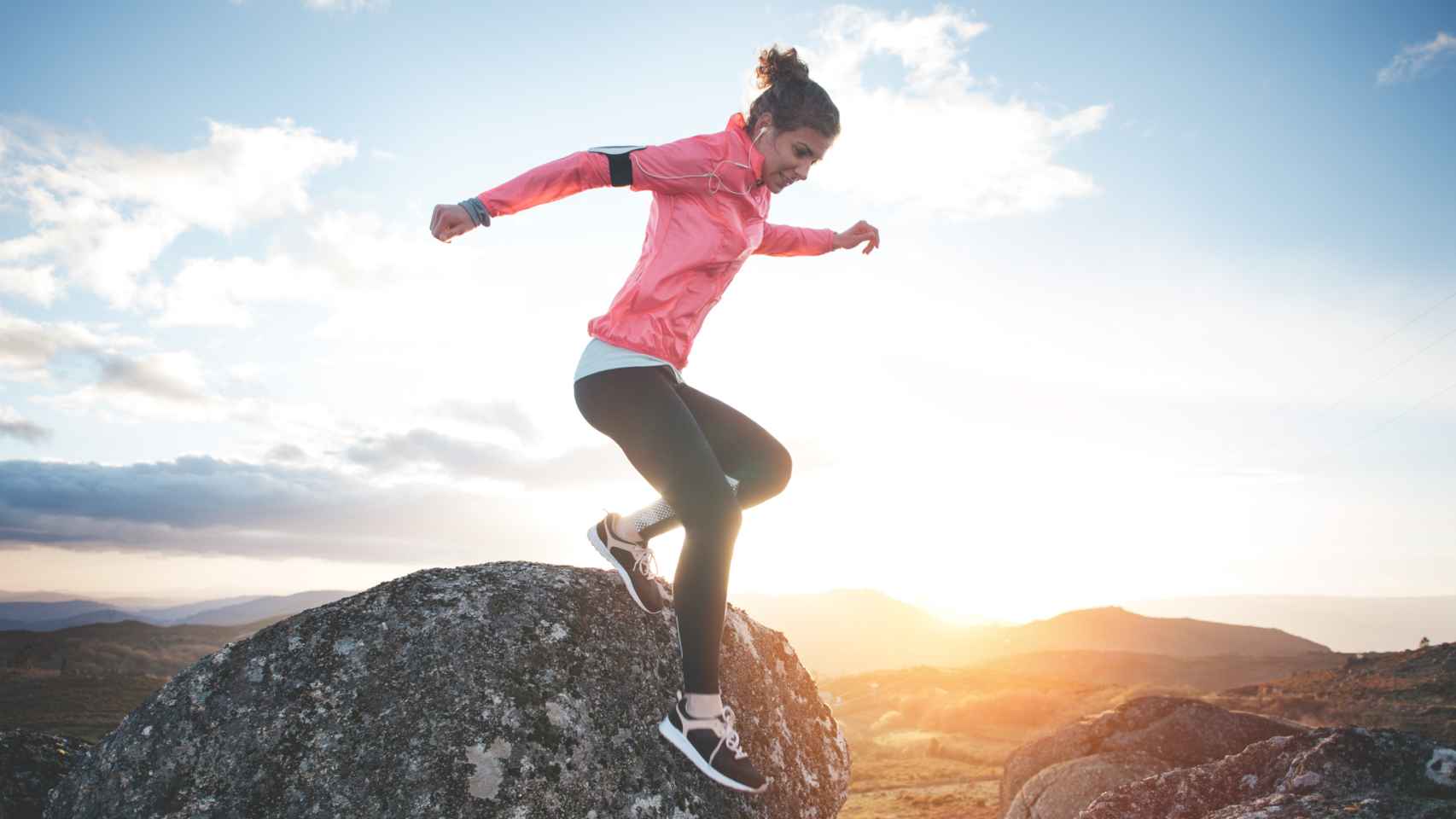 Una mujer hace ejercicio en la montaña mientras se pone el sol.